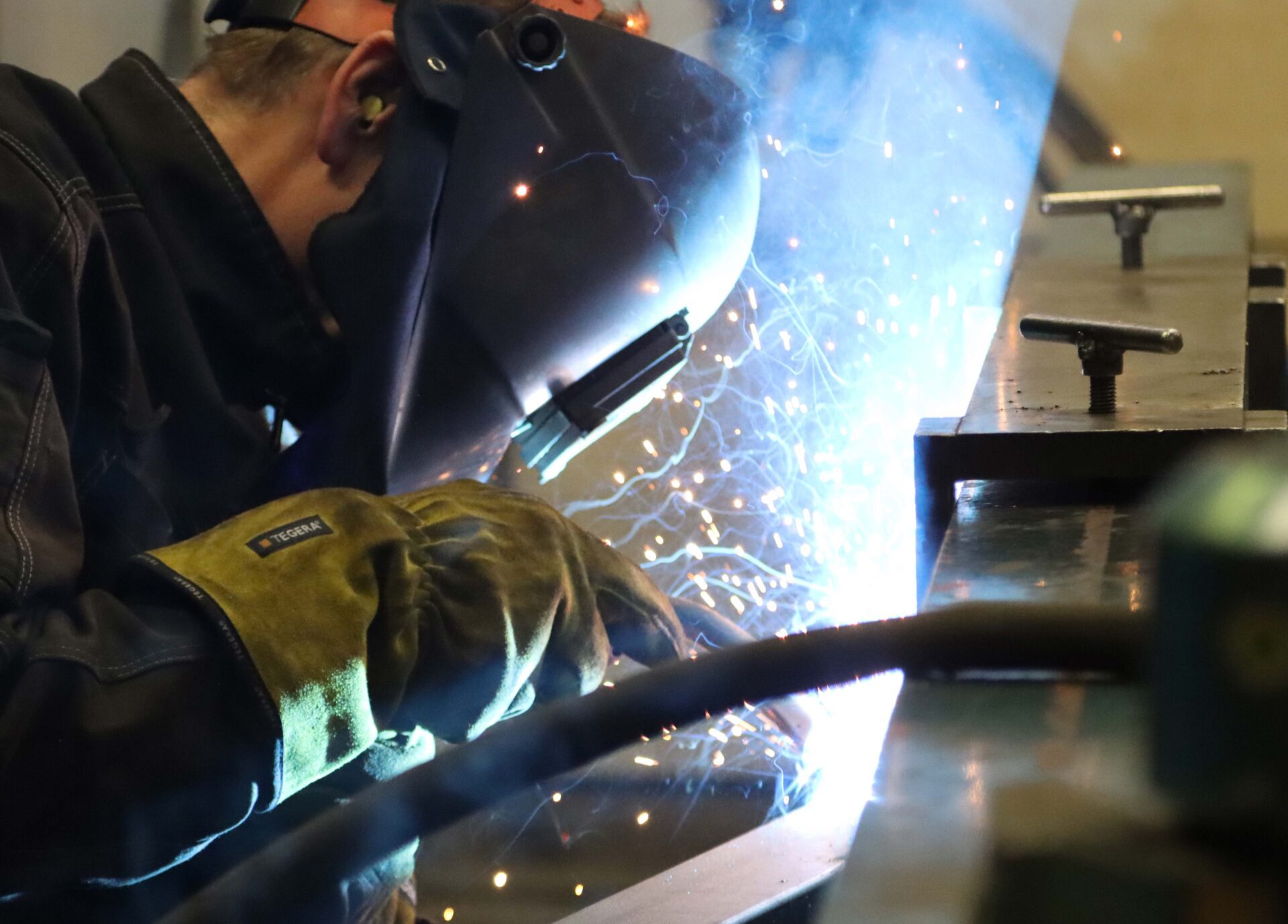 Man iförd svetshjälp svetsar på metallkonstruktion.